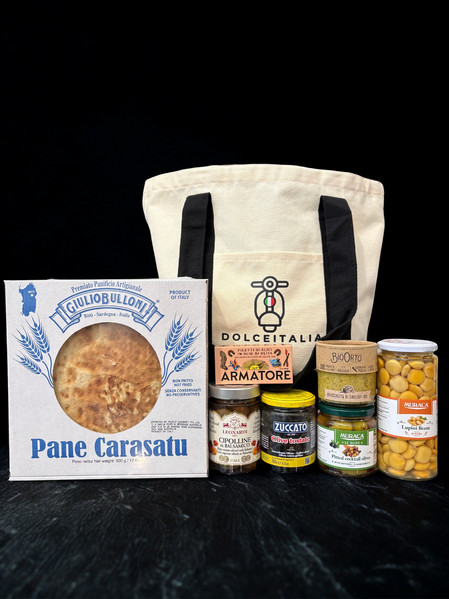 Collection of Italian food products including a bag, bread, and various jars on a black background. Italian gourmet hamper. Italian best gifts baskets 