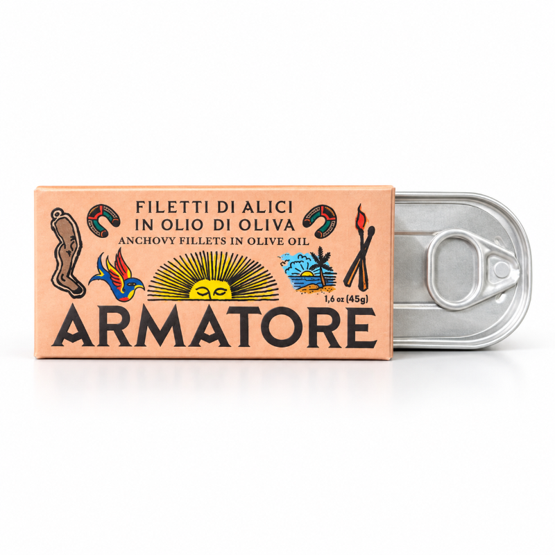A rectangular cardboard package labeled ARMATORE sits in front of an open silver pull-tab can, showing anchovy fillets in olive oil. The box is peach-toned with black text and small illustrated icons, photographed on a clean white background.Italian anchovy 
