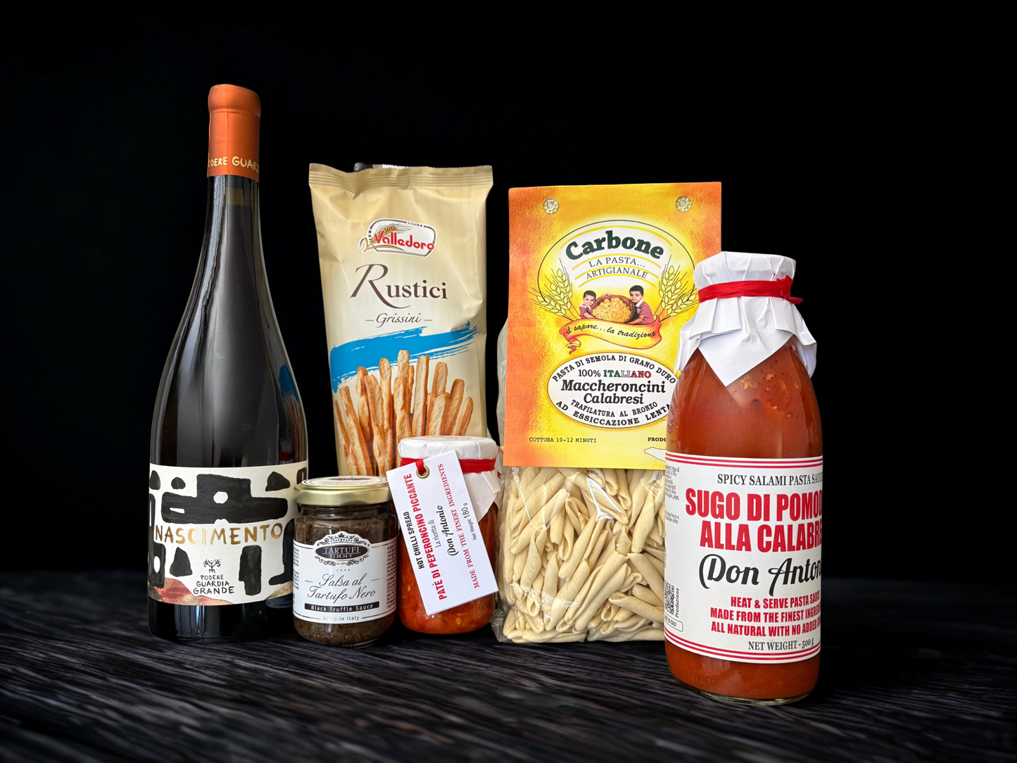 Collection of Italian food products including a bottle, pasta, and sauces on a black background. Italian gourmet Hampers delivered Australian wide. Italian Hamper Sunshine Coast